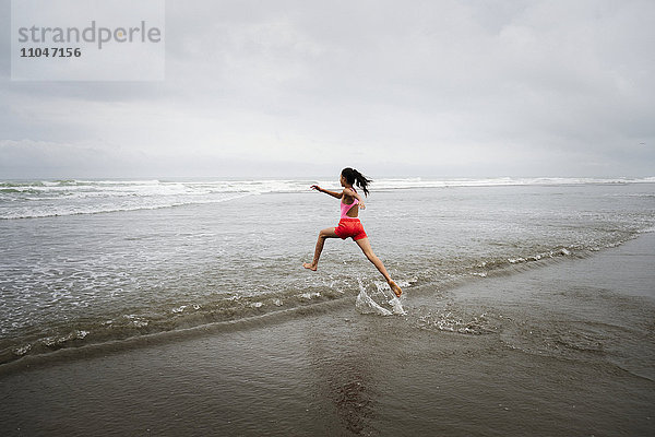 Gemischtrassiges Mädchen läuft am Strand ins Meer