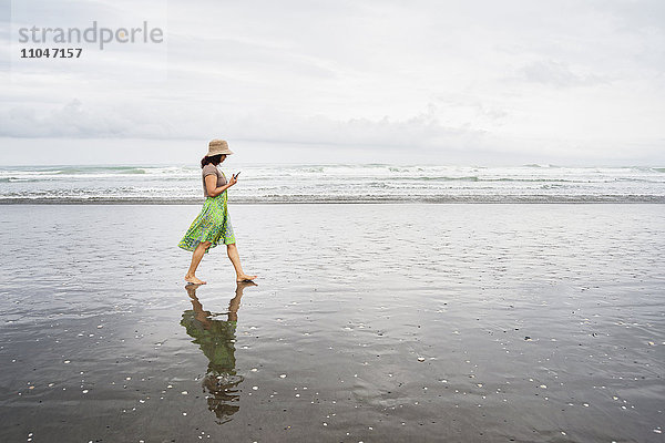Gemischtrassige Frau geht am Strand mit Handy