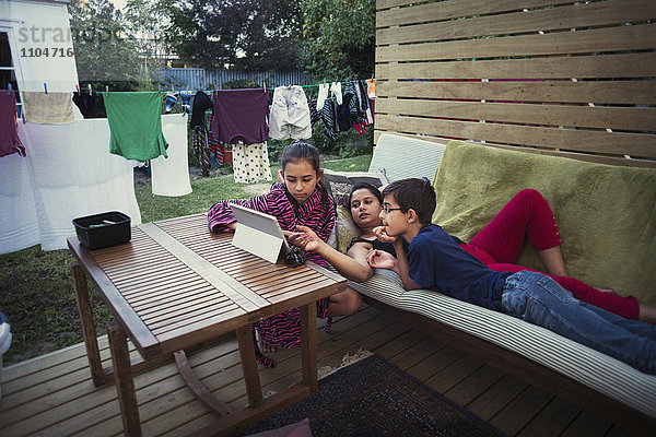 Mutter und Kinder benutzen ein digitales Tablet im Hinterhof
