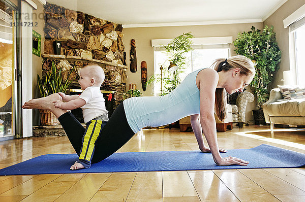 Mutter trainiert auf einer Übungsmatte mit Baby auf den Beinen