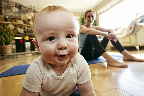 Baby krabbelt auf dem Boden  während die Mutter sich vom Training ausruht