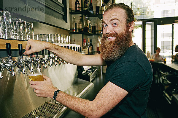 Lächelnder kaukasischer Barkeeper schenkt Bier ein