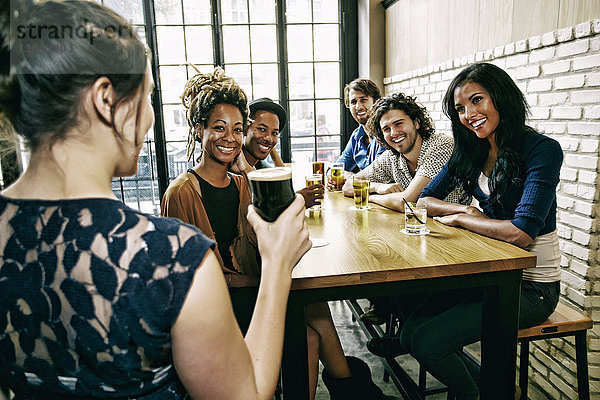 Kellnerin bedient lächelnde Freunde am Tisch in einer Bar