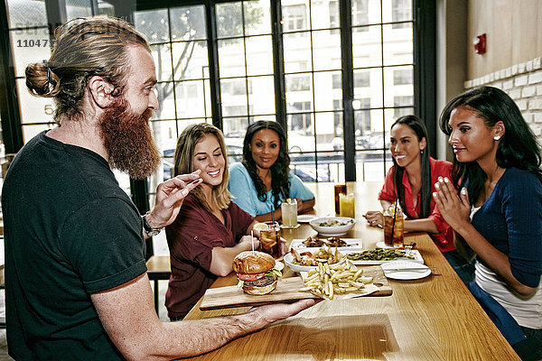 Kellner serviert Freunden am Tisch in einer Bar Speisen