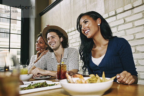Lächelnde Freunde  die an einem Tisch in einer Bar Essen und Cocktails genießen