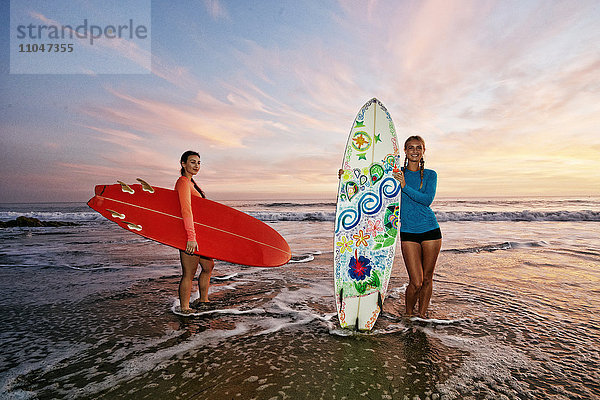 Frauen stehen in den Wellen des Ozeans und halten Surfbretter am Strand