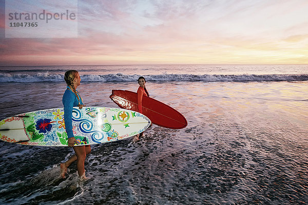 Frauen tragen Surfbretter in den Wellen des Ozeans am Strand