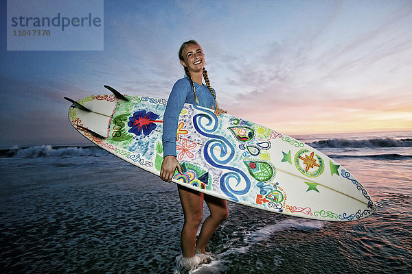 Kaukasische Frau mit Surfbrett am Strand