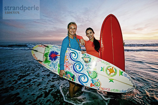 Frauen stehen in den Wellen des Ozeans und halten Surfbretter am Strand