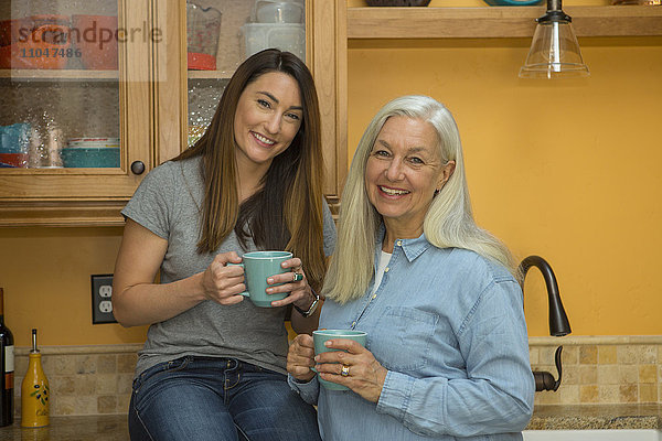 Kaukasische Frauen posieren in der Küche und trinken Kaffee