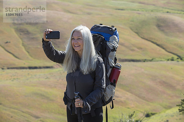 Ältere kaukasische Frau beim Wandern mit Rucksack  die ein Selfie macht