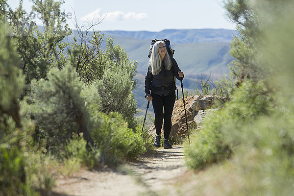 Ältere kaukasische Frau beim Wandern mit Rucksack auf einem Pfad