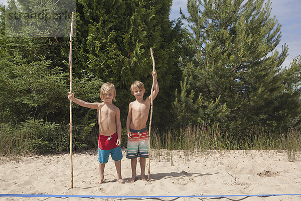 Kaukasische Jungen halten Stöcke am Strand