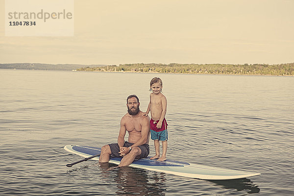 Kaukasischer Vater und Sohn auf einem Paddelbrett im See