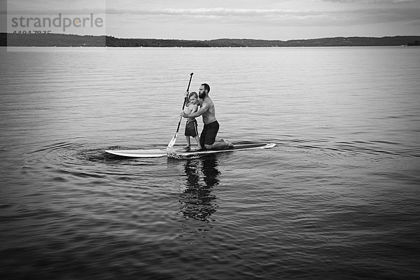 Kaukasischer Vater und Sohn auf einem Paddelbrett im See