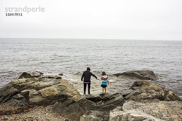 Kaukasische Mutter und Tochter halten sich auf Felsen am Meer an den Händen