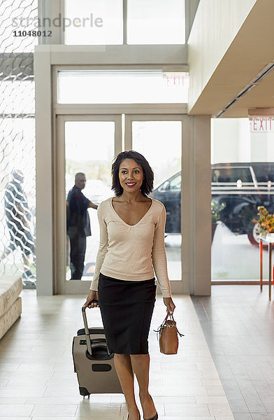 Afroamerikanische Geschäftsfrau rollt Gepäck in der Hotellobby
