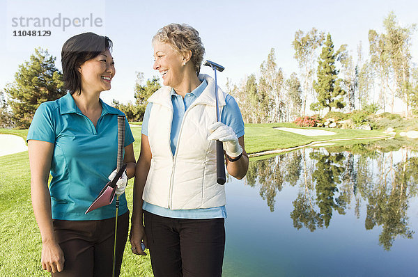 Lachende Frauen auf dem Golfplatz in der Nähe des Wasserhindernisses