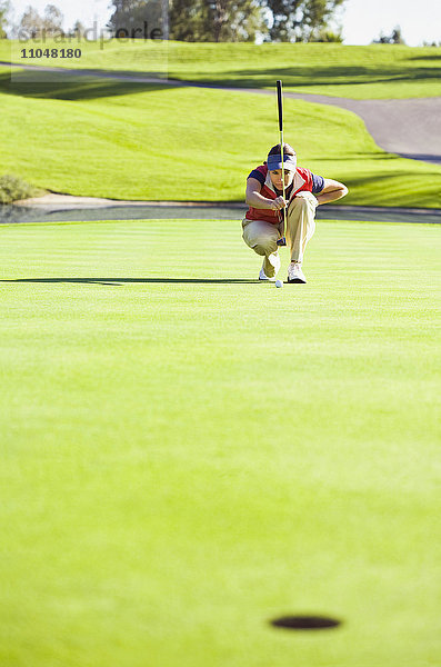 Kaukasische Frau plant Putt auf dem Grün eines Golfplatzes