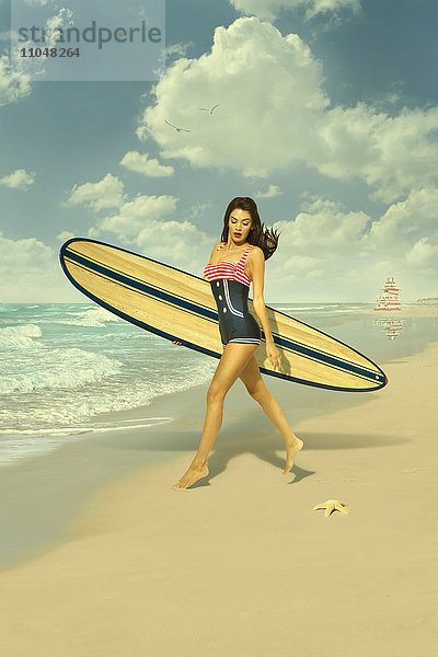 Kaukasische Frau läuft am Strand und trägt ein Surfbrett
