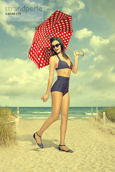 Kaukasische Frau hält gepunkteten Regenschirm am Strand