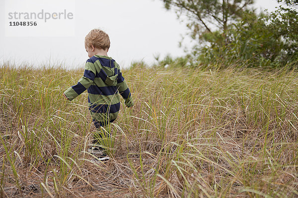 Kaukasischer Junge  der in einem Feld mit hohem Gras läuft