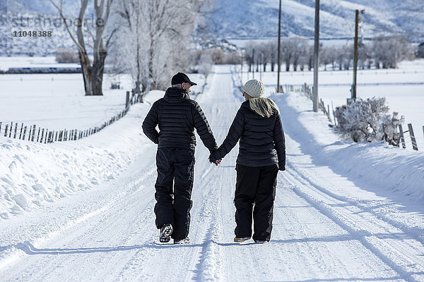 Kaukasisches Paar geht auf verschneiter  abgelegener Straße spazieren