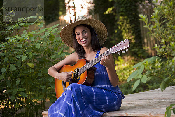 Lachende hispanische Frau spielt Gitarre auf der Terrasse im Hinterhof