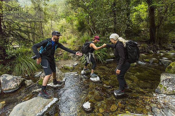 Kaukasische Wanderer überqueren einen Bach auf Felsen im Wald