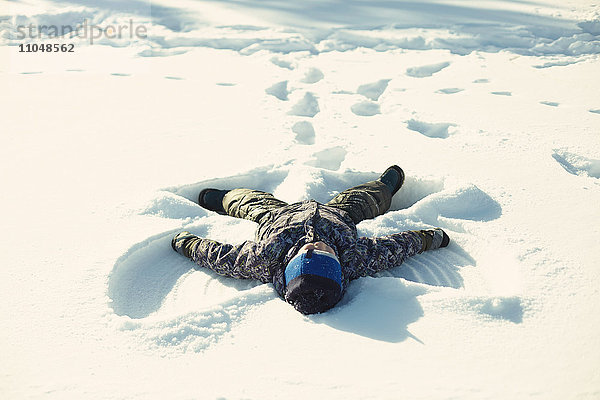 Kaukasischer Junge macht Schneeengel