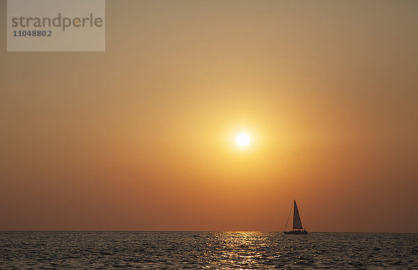 Segelboot segelt bei Sonnenuntergang am Meereshorizont
