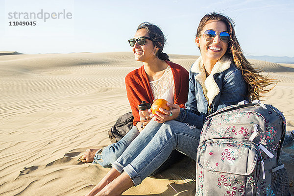 Gemischtrassige Frauen sitzen auf Sanddünen