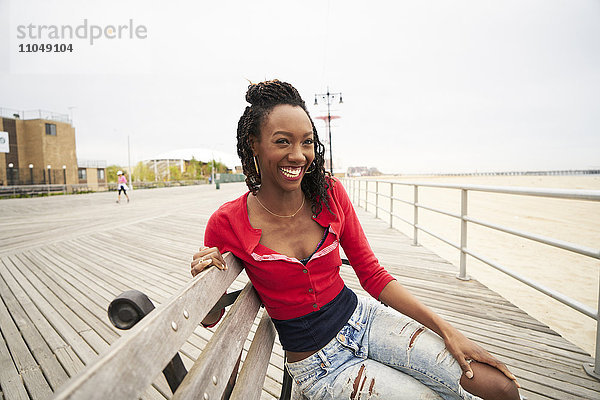 Schwarze Frau lächelnd auf Bank an der Promenade