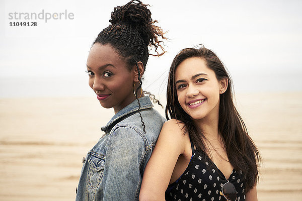 Lächelnde Frauen Rücken an Rücken am Strand