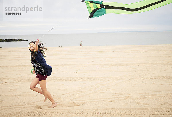 Mixed Race Frau läuft am Strand fliegender Drachen