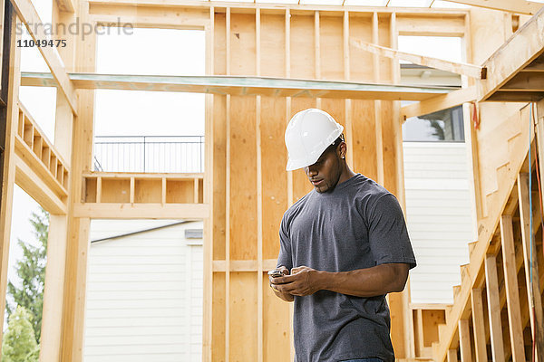 Schwarzer Bauarbeiter schreibt eine SMS mit seinem Handy