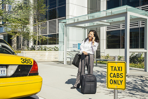 Geschäftsfrau  die in der Nähe eines Taxis mit einem Handy telefoniert