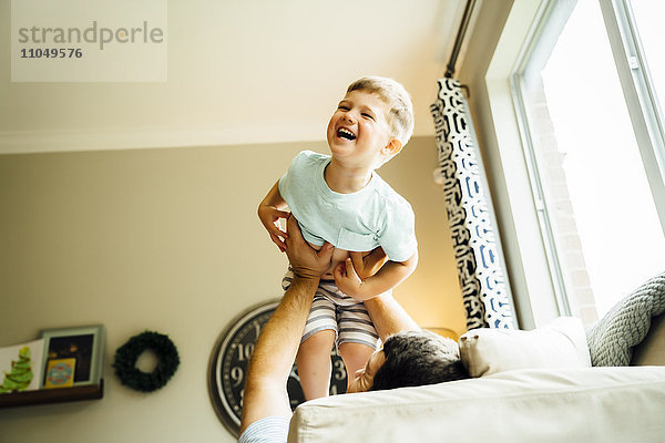 Kaukasischer Vater liegt auf dem Sofa und hebt seinen Sohn hoch