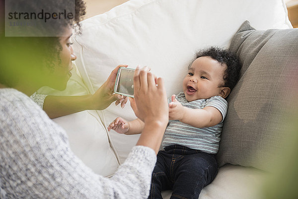 Mutter fotografiert Babysohn mit Handy auf Sofa