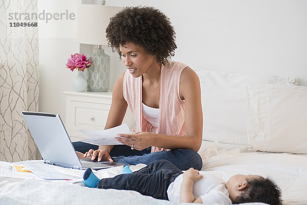 Mutter bezahlt Rechnungen auf dem Laptop mit ihrem kleinen Sohn im Bett