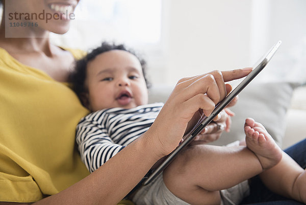 Mutter hält ihren kleinen Sohn und benutzt ein digitales Tablet