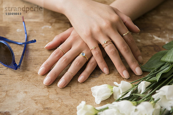 Hände einer hispanischen Frau mit Ringen in der Nähe von Blumen und Sonnenbrille