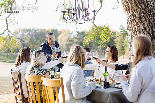 Freunde stoßen am Tisch im Freien mit Wein an