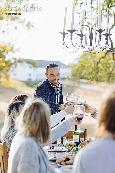 Freunde stoßen am Tisch im Freien mit Wein an