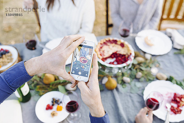 Kaukasischer Mann fotografiert Essen an einem Tisch im Freien