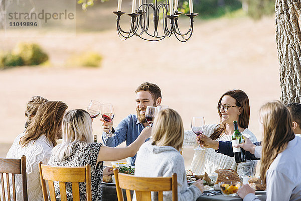 Freunde stoßen am Tisch im Freien mit Wein an