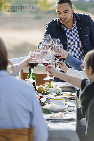 Freunde stoßen am Tisch im Freien mit Wein an