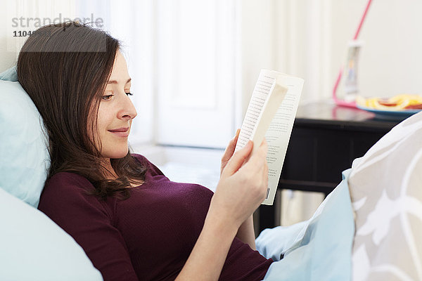 Gemischtrassige Frau liest Buch im Bett