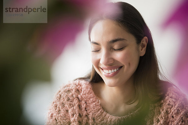 Hispanische Frau lächelnd hinter rosa Blumen