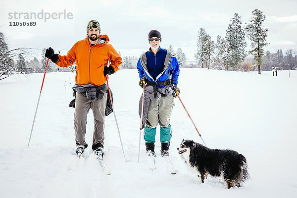 Kaukasisches Paar und Hund beim Skilanglauf auf einem verschneiten Feld